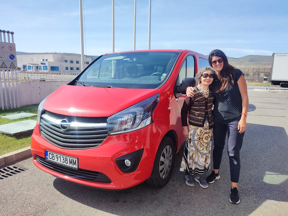 A private tour guide posing with a nice tourist next to a red van, smiling and enjoying their time together.