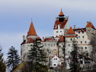 Bran Castle, famously associated with the Dracula legend, standing majestically with its red rooftops against a cloudy sky backdrop.