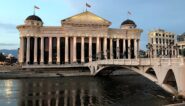 Neoclassical building and old stone bridge reflected in a river in Skopje, North Macedonia.