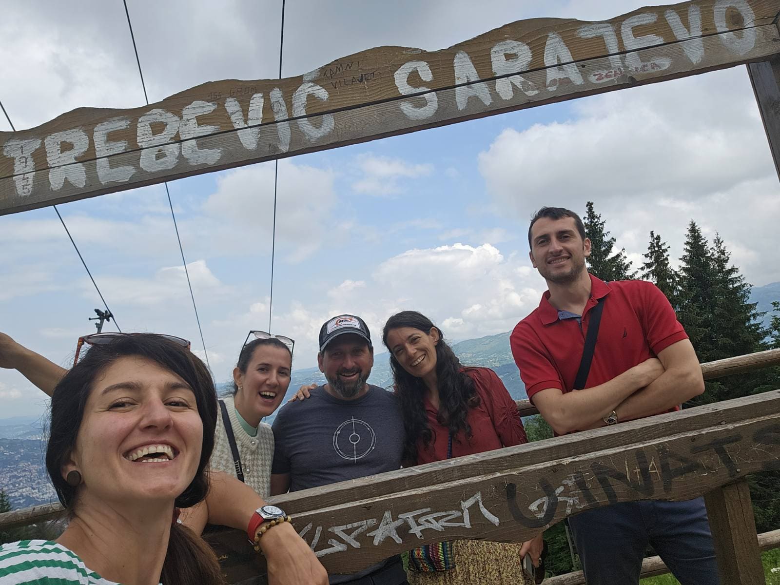 A group of tourists posing in front of a historical site in Sarajevo, with a scenic background of the city and mountains.